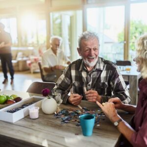 An older man and woman in senior living smile as they put together a puzzle.